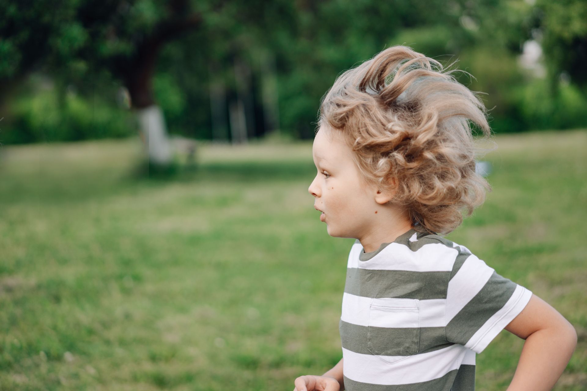 Child running through grass in a striped shirt, with a house and bushes in the background