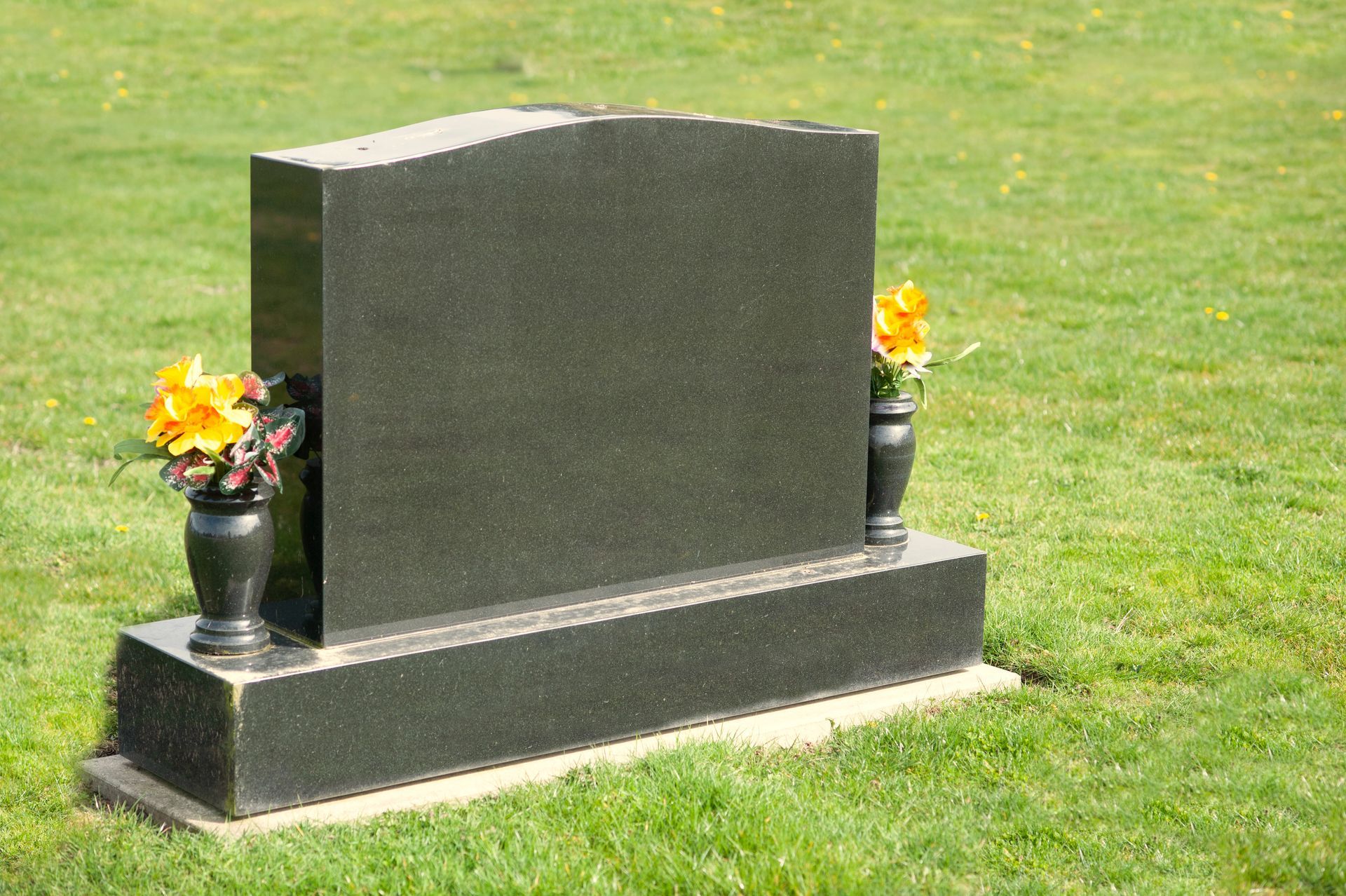 A large tombstone with vases and flowers with space for a message on green grass A large tombstone with vases and flowers with space for a message on green grass
