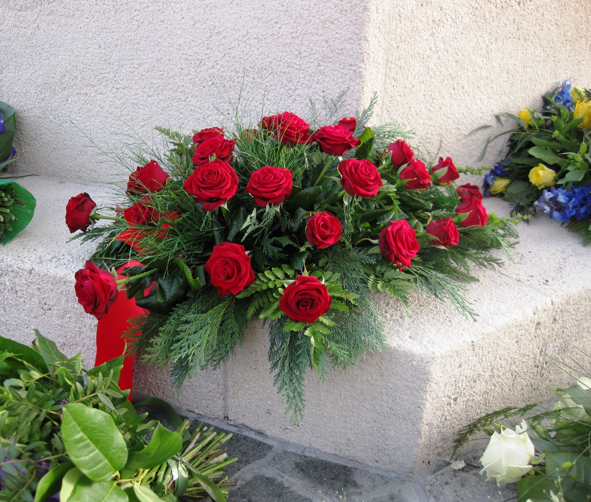 Arrangement of red roses and green foliage on a stone surface, likely a memorial.