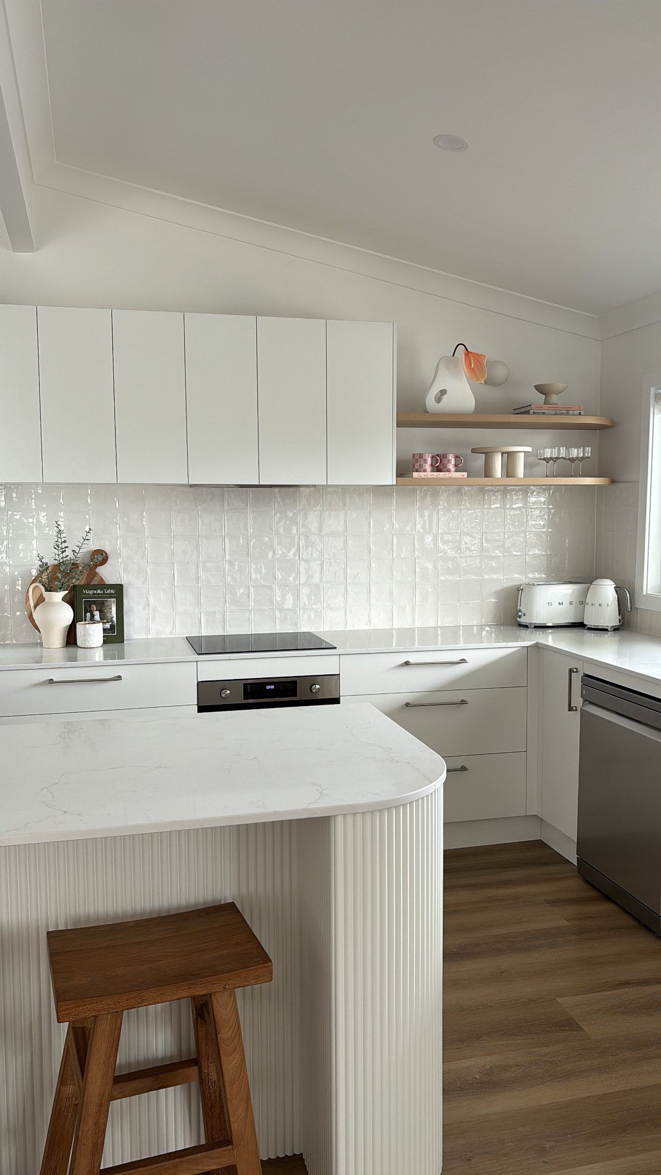 A kitchen with white cabinets , a wooden stool , a stove , and a dishwasher.