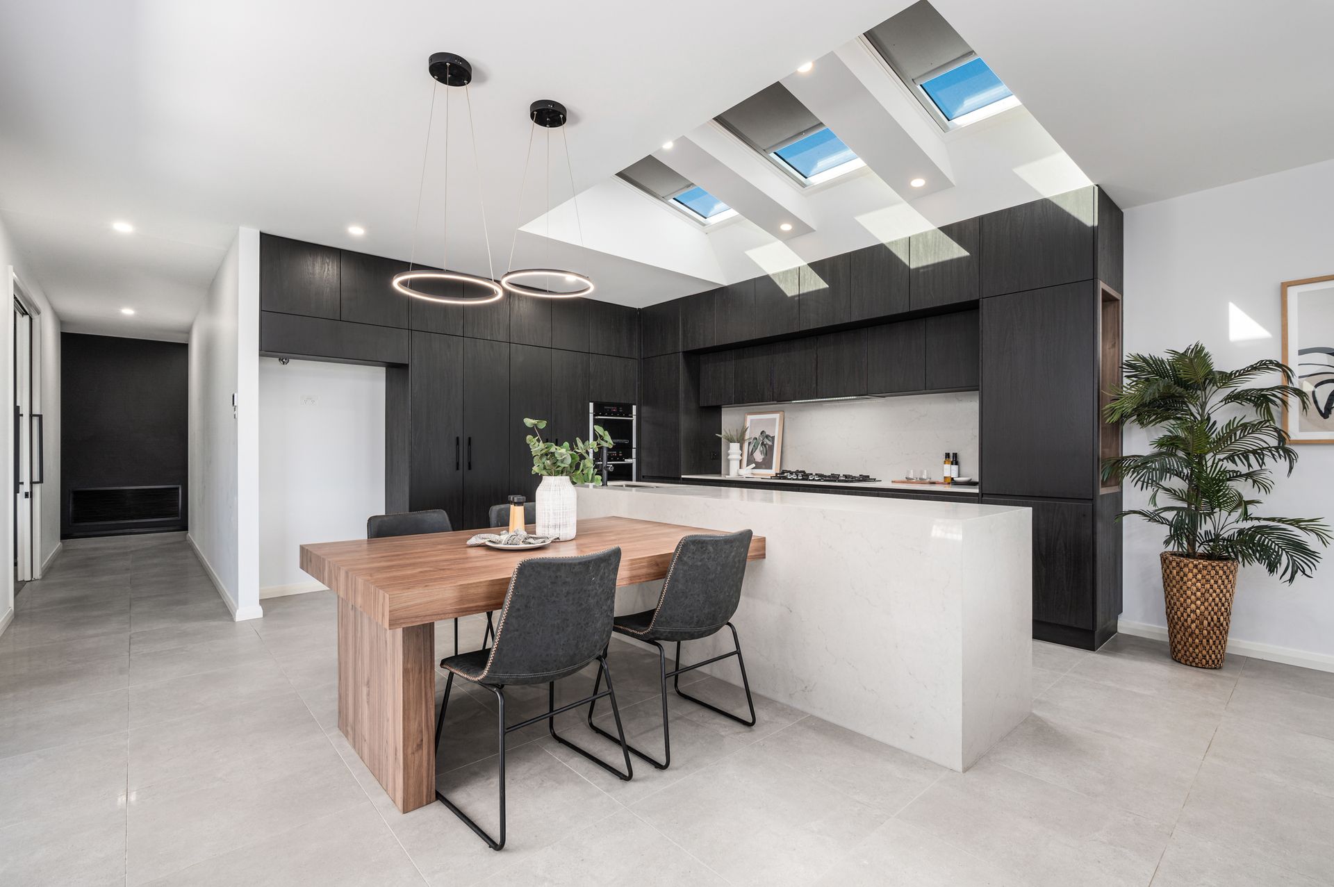 Modern kitchen with black cabinetry, white island, wooden table, and skylights - - Groves Joinery NSW