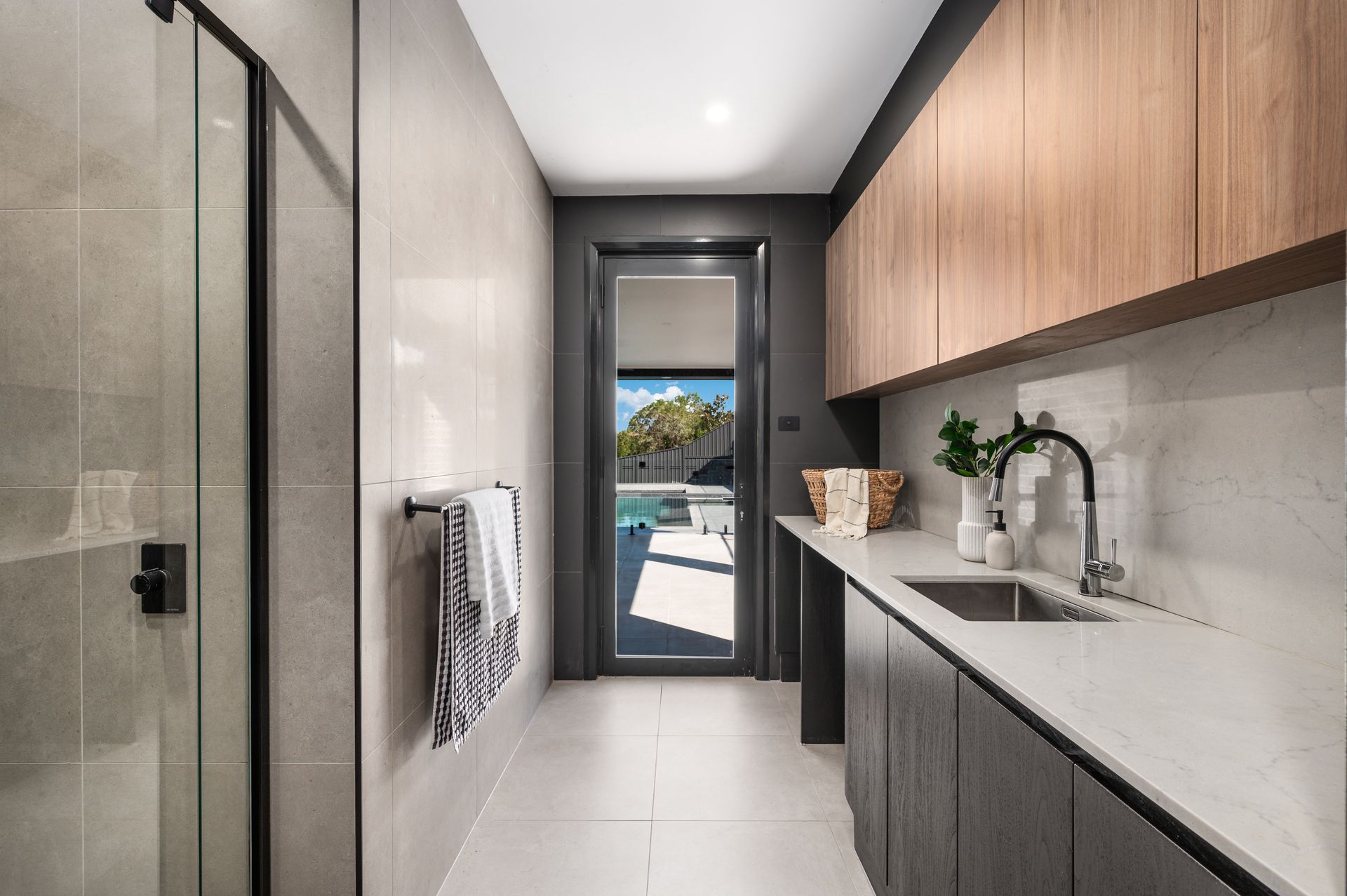 Modern laundry room with gray and wood cabinets, a sink, and a view of a pool - Groves Joinery NSW