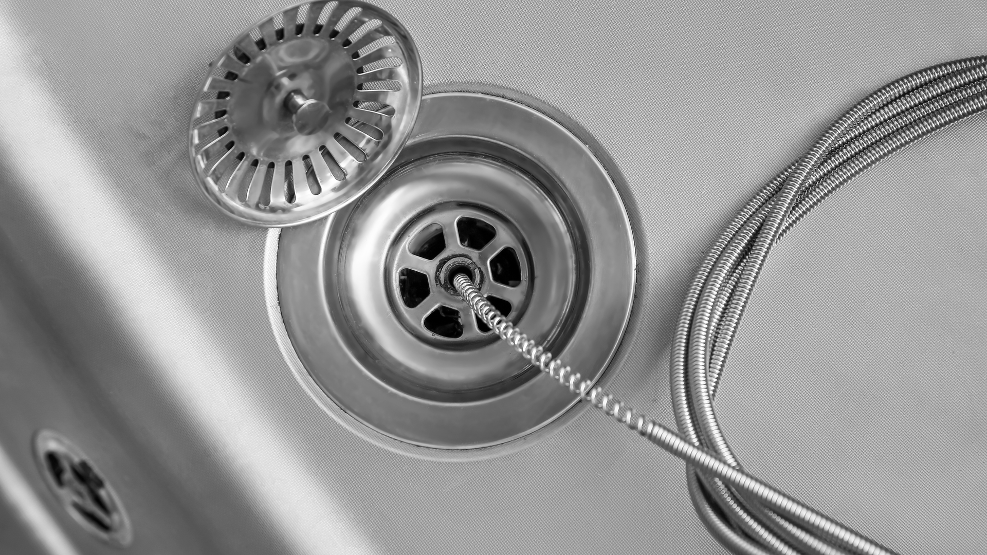 Close-up of a metal sink drain with a strainer and coiled wire inside the basin.