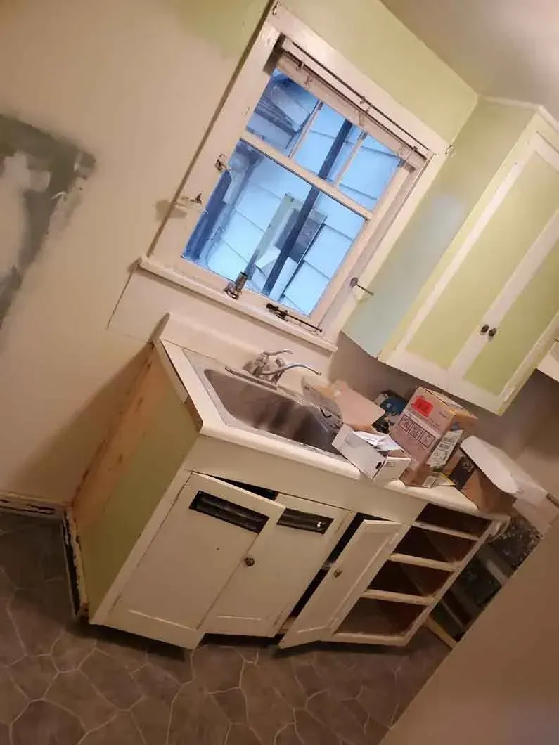 Small kitchen with white cabinets, sink under a window, and tiled floor at a slight angle.