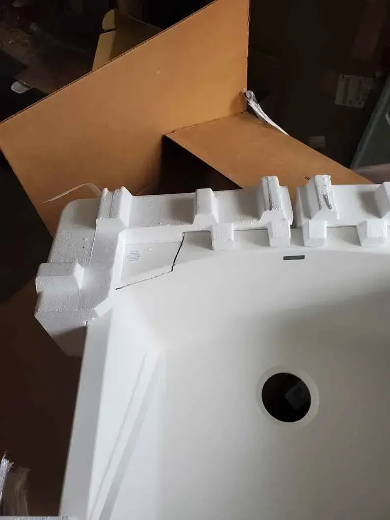 White foam packaging with a circular hole, sitting in front of an open brown cardboard box.