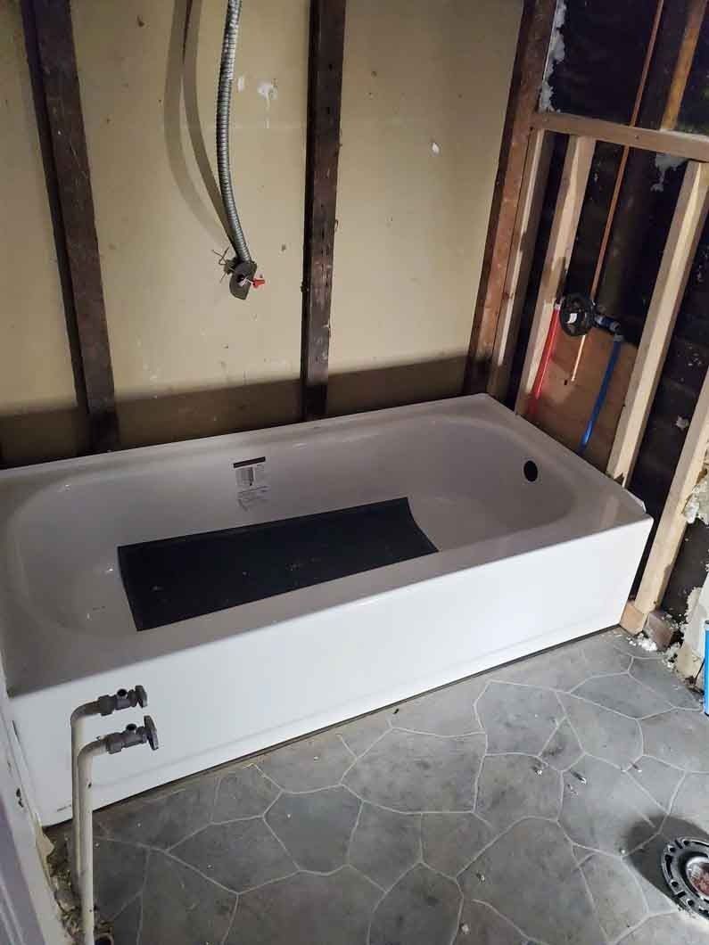 White bathtub installed in an unfinished bathroom with exposed wall studs and plumbing.