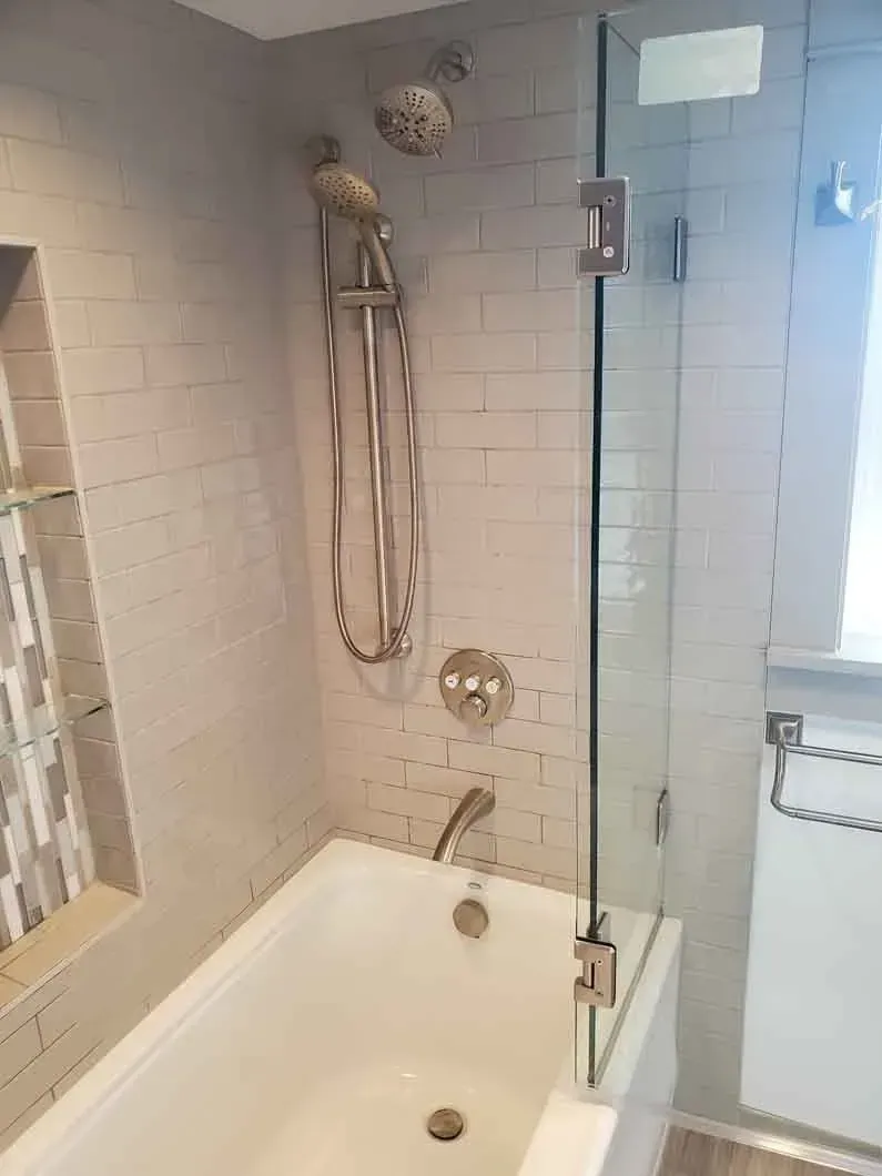 Bathroom with a bathtub, wall-mounted showerhead, and tiled walls near a window.