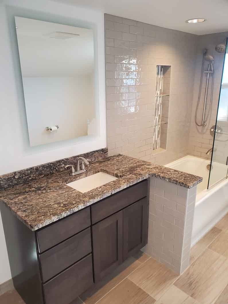 Modern bathroom vanity with granite countertop, vessel sink, mirror, and glass shower tiles.
