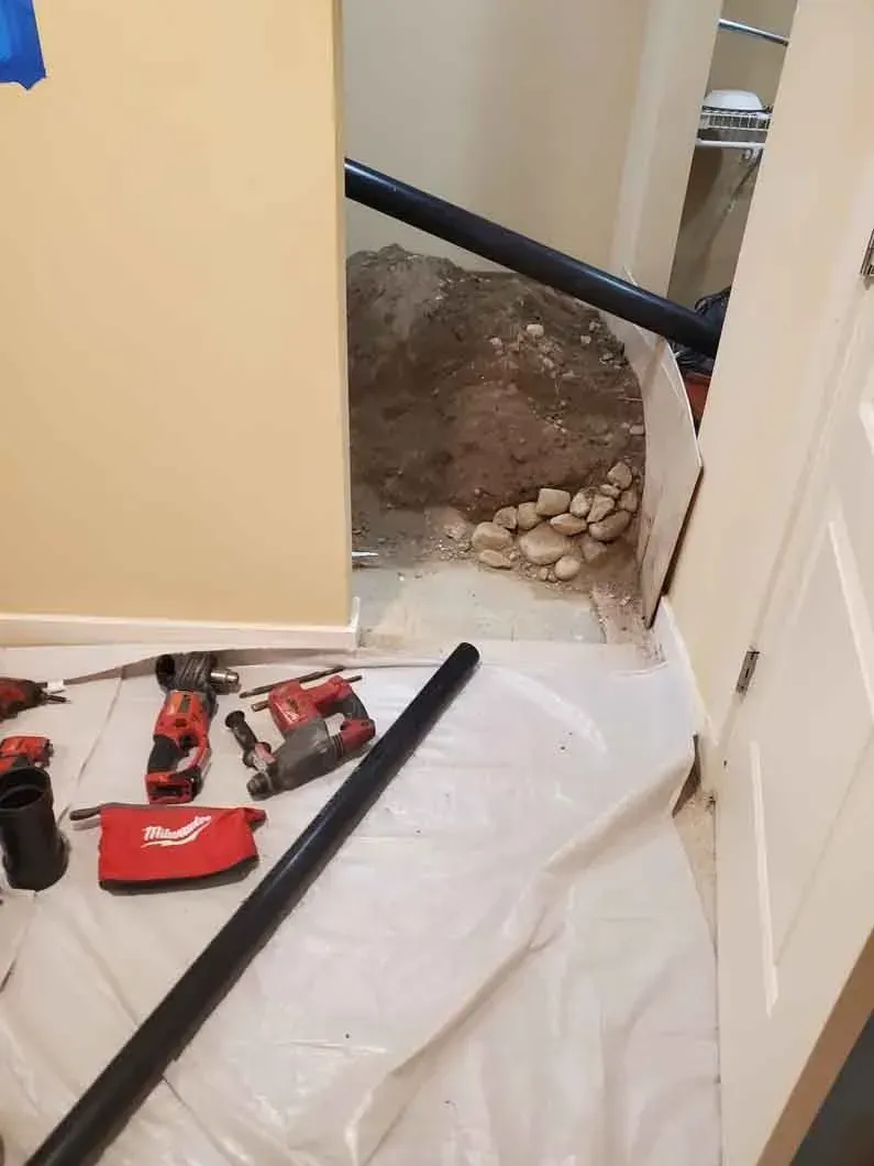 Interior doorway with exposed floor hole, dirt, and tools on a plastic sheet during renovation