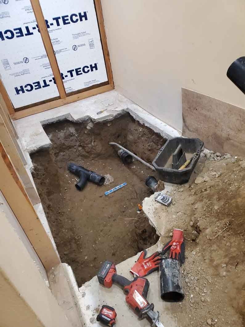 Indoor floor under construction with exposed dirt, tools, and red power drills near a window.