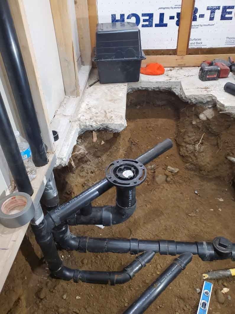 Plumbing pipes and a valve exposed in a dug-out trench beside a house foundation under repair