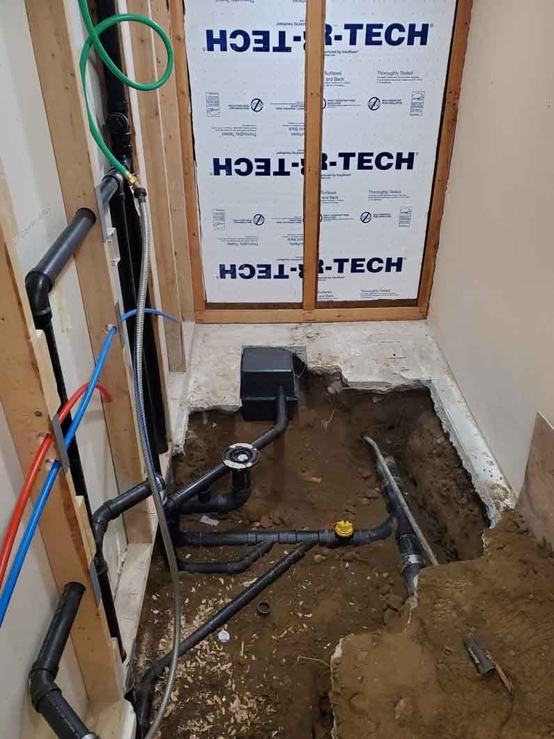 Bathroom under renovation with exposed plumbing, dirt floor, and insulation-covered wall framing