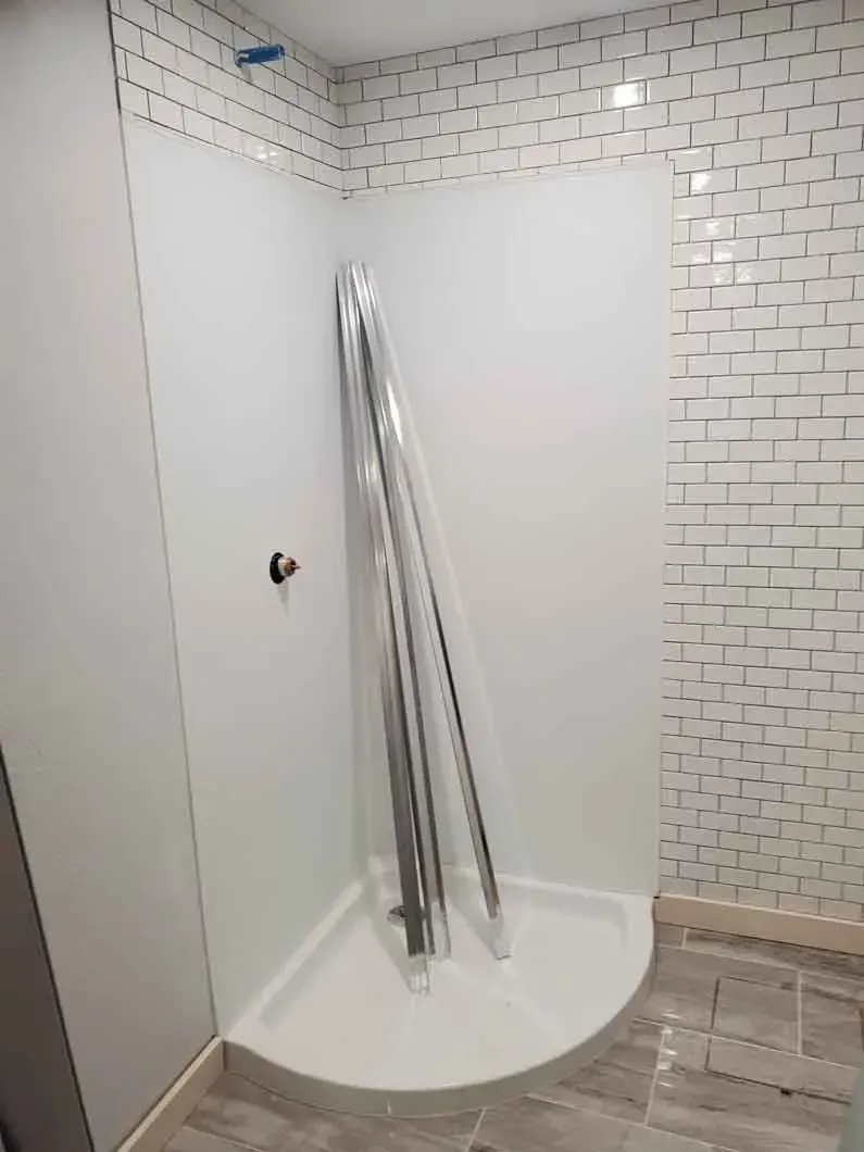 Empty tiled shower with a curved white base and metal rails leaning against the wall.