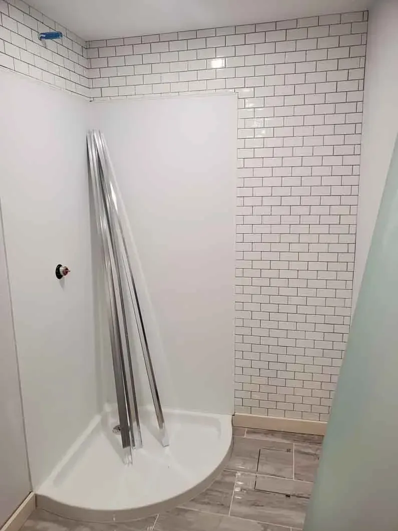 Small tiled shower room with a white shower base, leaning metal rods, and a brick-patterned wall