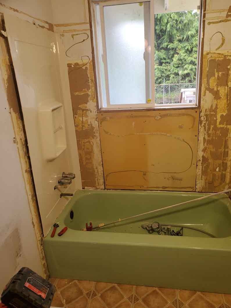 Partially renovated bathroom with a green bathtub, unfinished walls, and a window above the tub