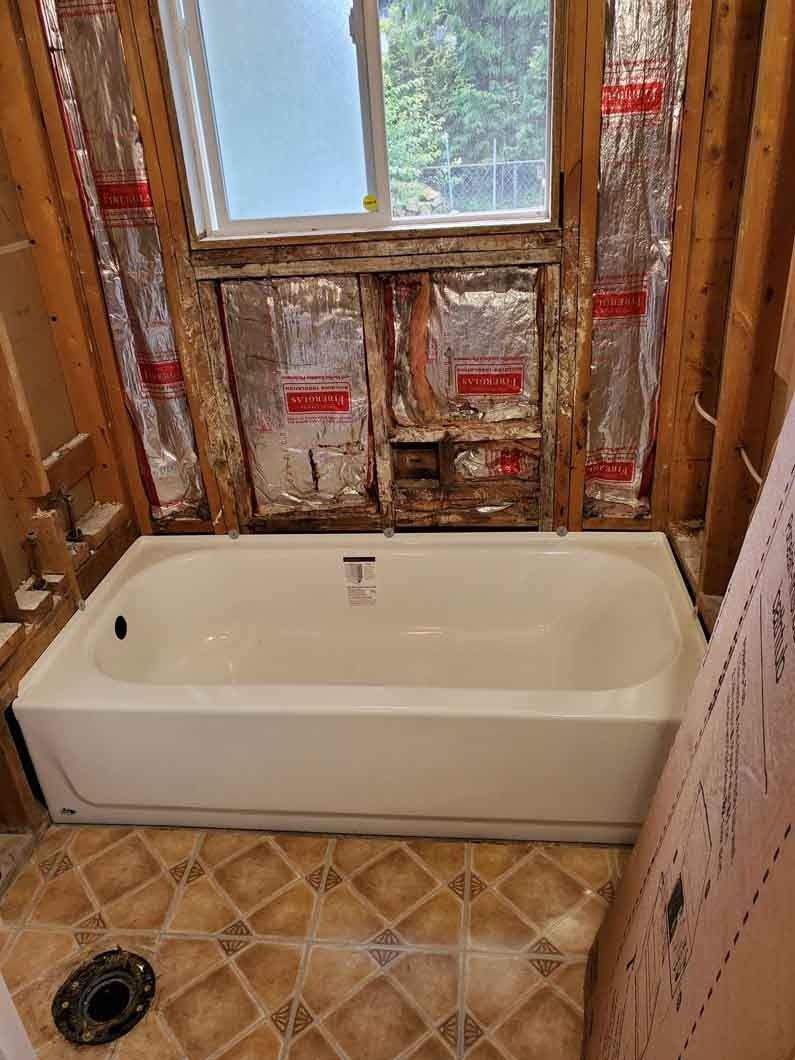 Partially renovated bathroom with bathtub, exposed wall studs, and tiled floor