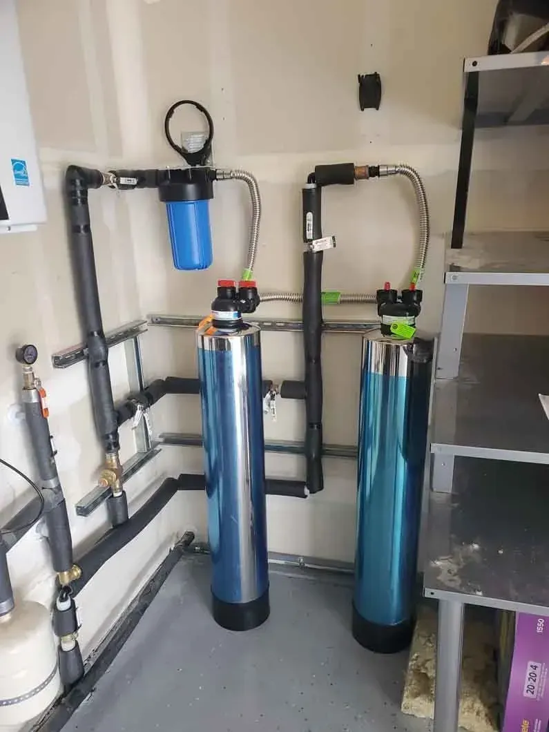 Water treatment system with two blue cylindrical tanks and black piping in a utility room