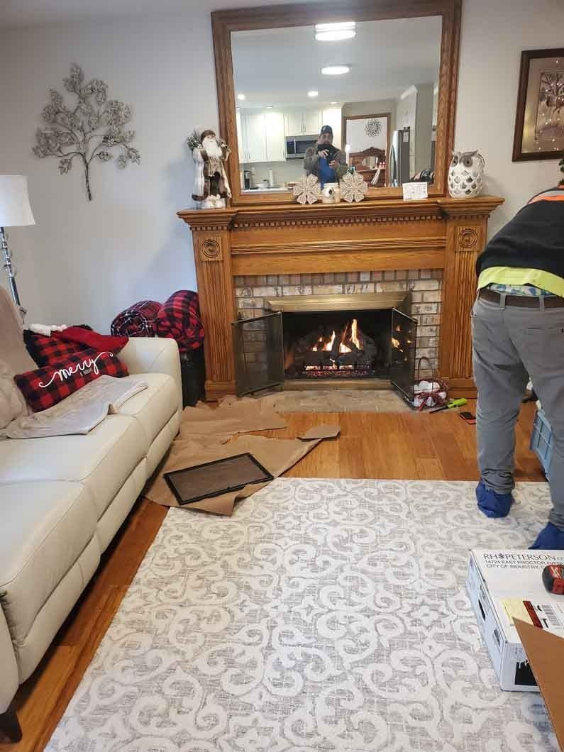 Living room with fireplace and mirror, with a person standing near the hearth and a couch on the left.