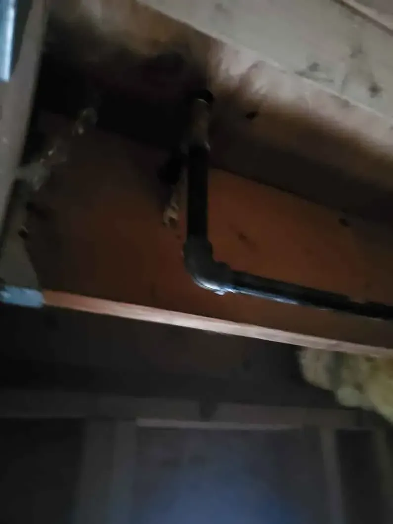 Close-up of dark pipes beneath a wooden surface, with a small metal elbow joint visible.
