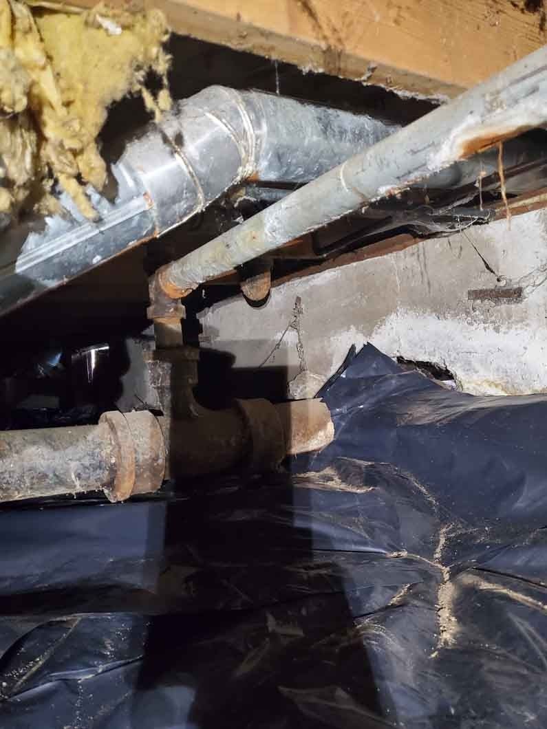 Exposed metal pipes and ductwork in a crawl space with insulation and black plastic sheeting