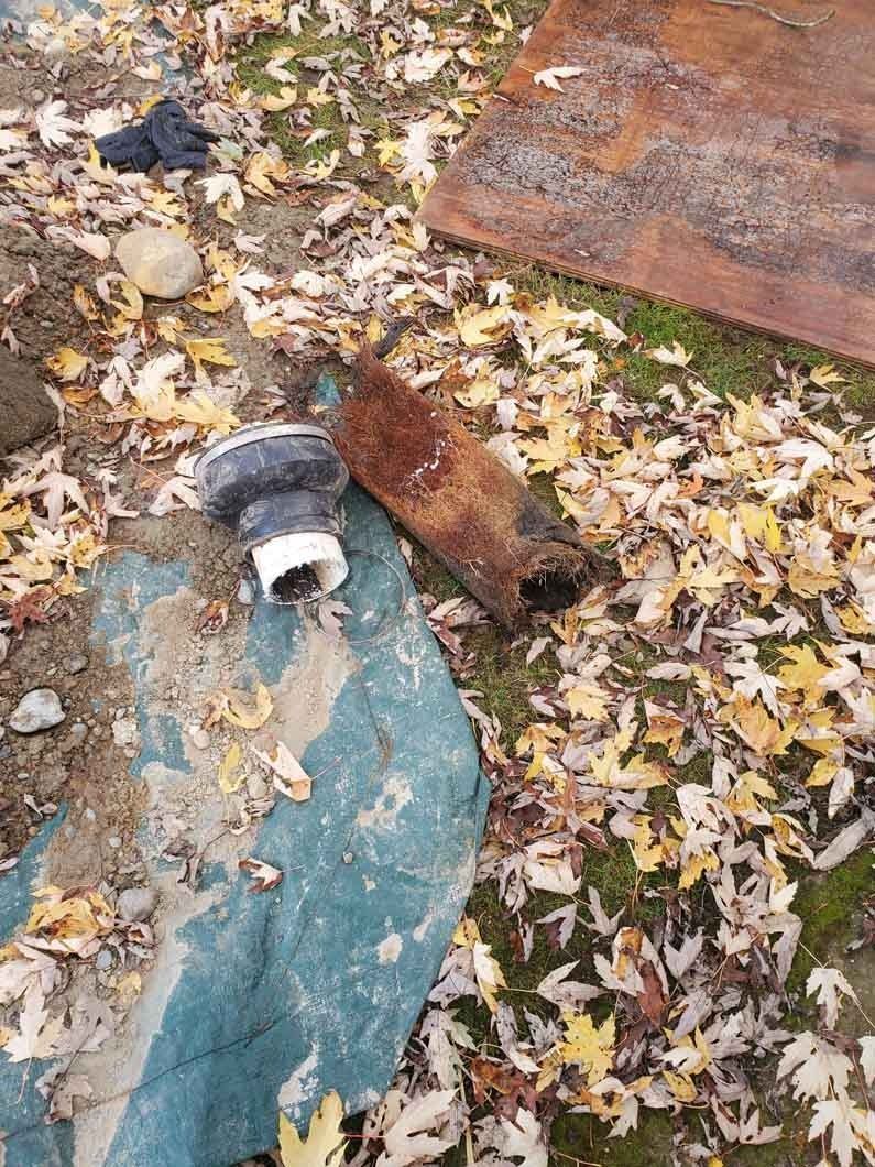 Leaf-covered ground with a small gray pipe and blue tarp beside rusty metal sheets