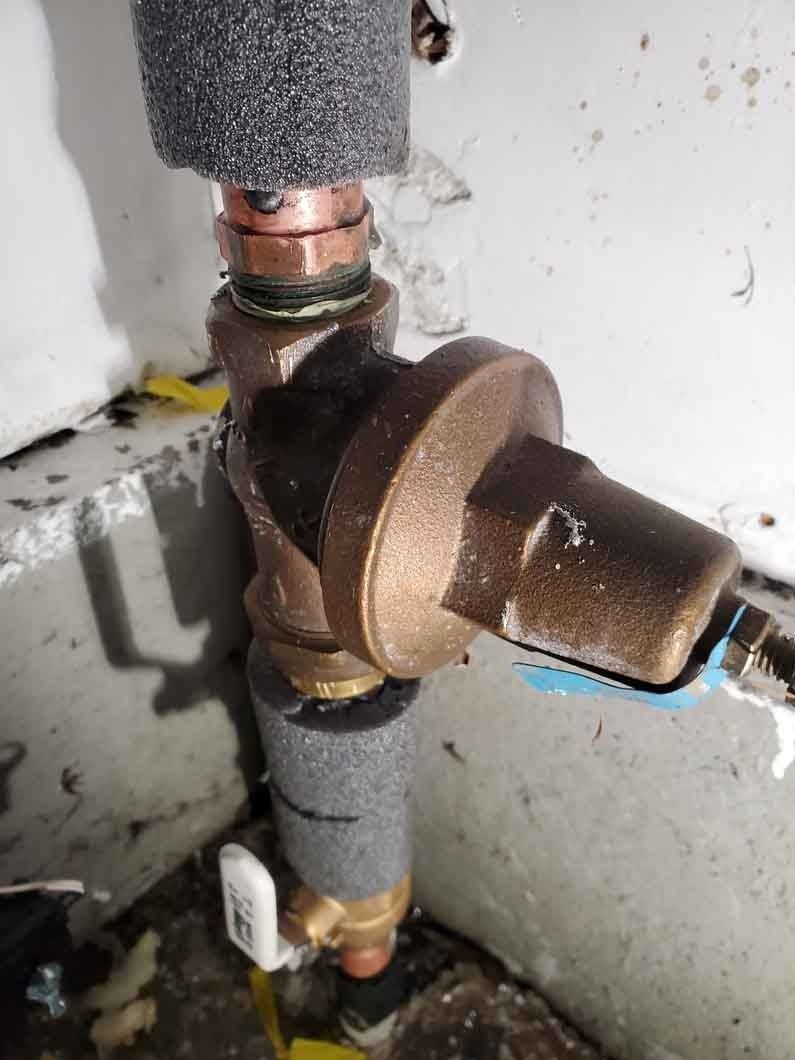 Close-up of a brass pipe valve and fittings connected to gray insulated plumbing in a wall cavity
