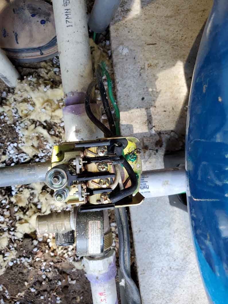 Close-up of a rusty pipe valve and fittings beside a blue tank on a dusty floor