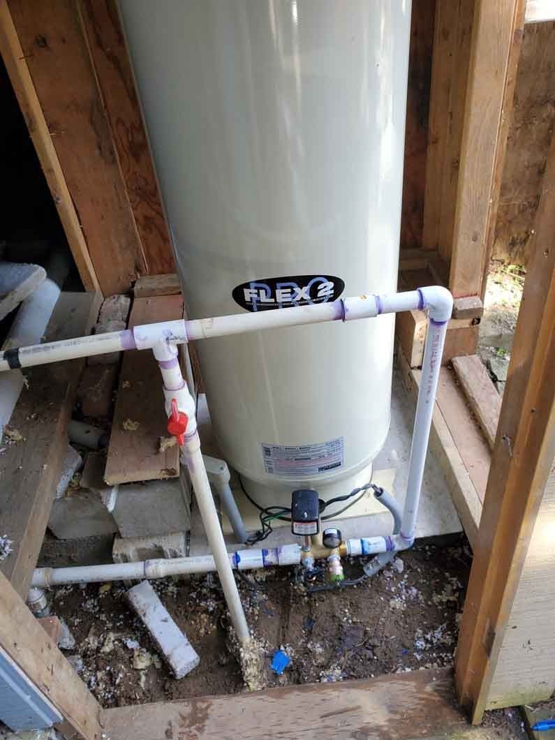 Water heater with PVC plumbing in an unfinished basement framed by wooden studs.