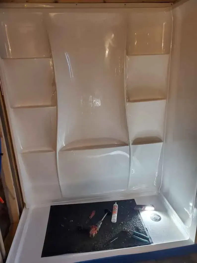 White shower stall with built-in shelves and a black drain cover at the bottom.