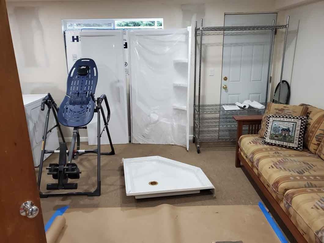Home workout room with a chair-style exercise machine, foam mat, sofa, and shelving.