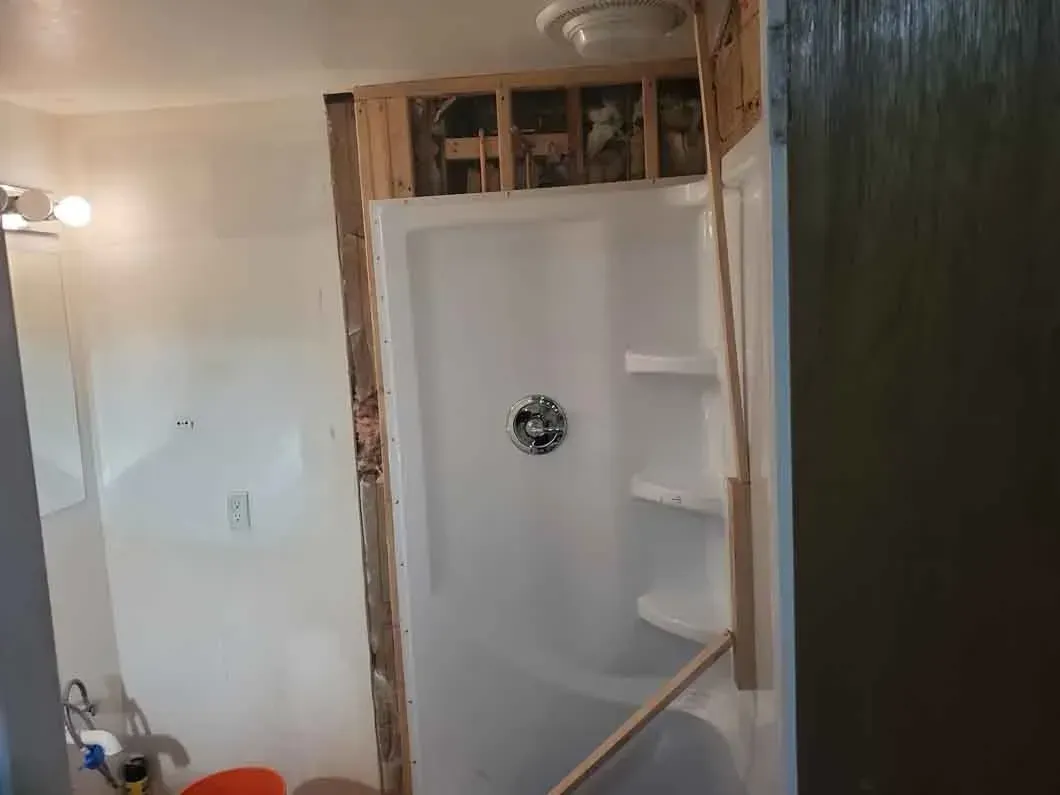 Bathroom shower under renovation, with exposed framing around a white shower stall.