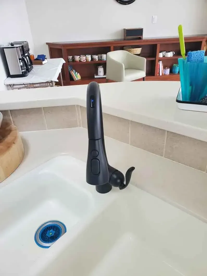 Kitchen sink with black faucet, white countertop, blue drain, and a blue utensil holder in the background