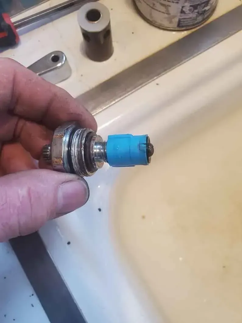 Hand holding a small metal valve with a blue plastic top over a sink or countertop