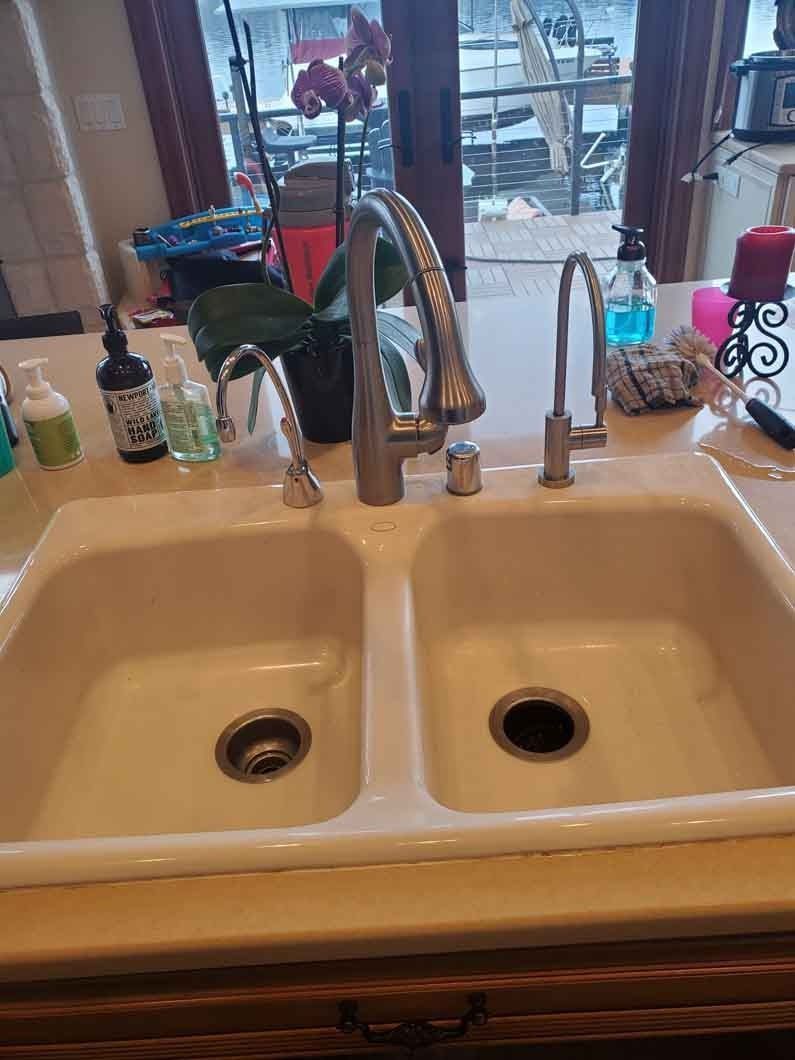 Kitchen double sink with faucet, bottles, and a sponge near a window.