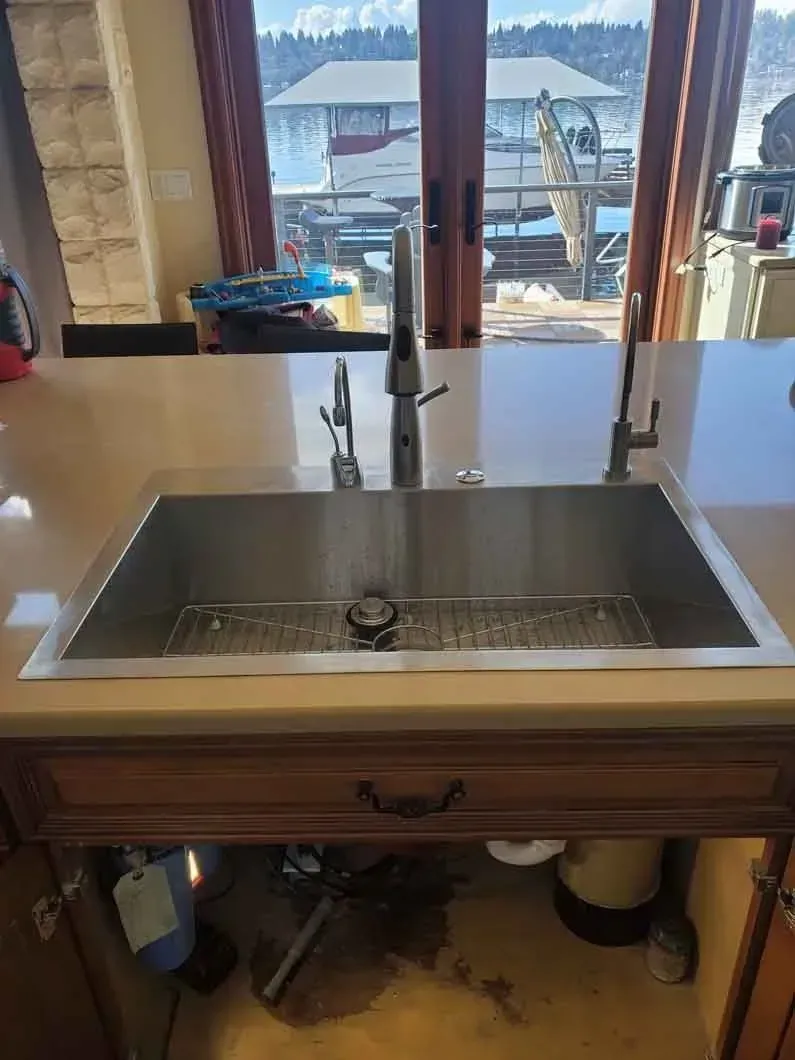 Kitchen sink with faucet and countertop, looking out to a snowy waterfront view through glass doors.