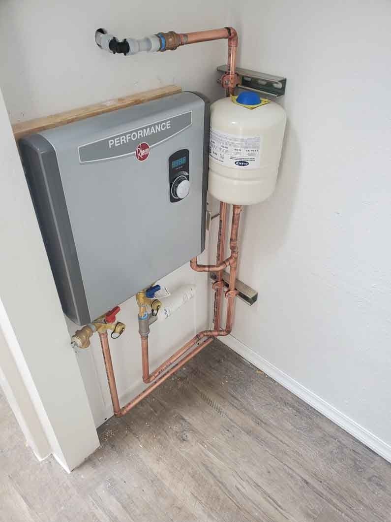 Wall-mounted heating or boiler unit with copper pipes and a white tank in a small utility closet