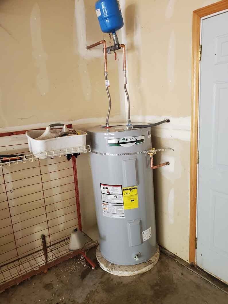 Water heater in a utility room with exposed pipes, a blue expansion tank, and a laundry sink.