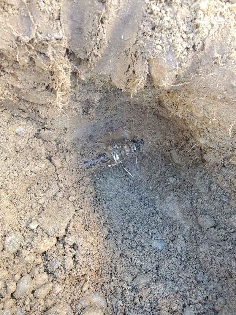Freshly dug hole in dry dirt with a small pool of muddy water at the bottom