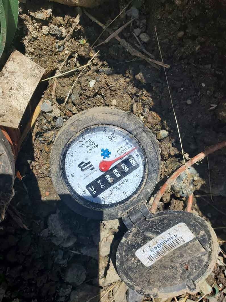 Water meter lids in dirt, one open showing a white dial with red numbers.