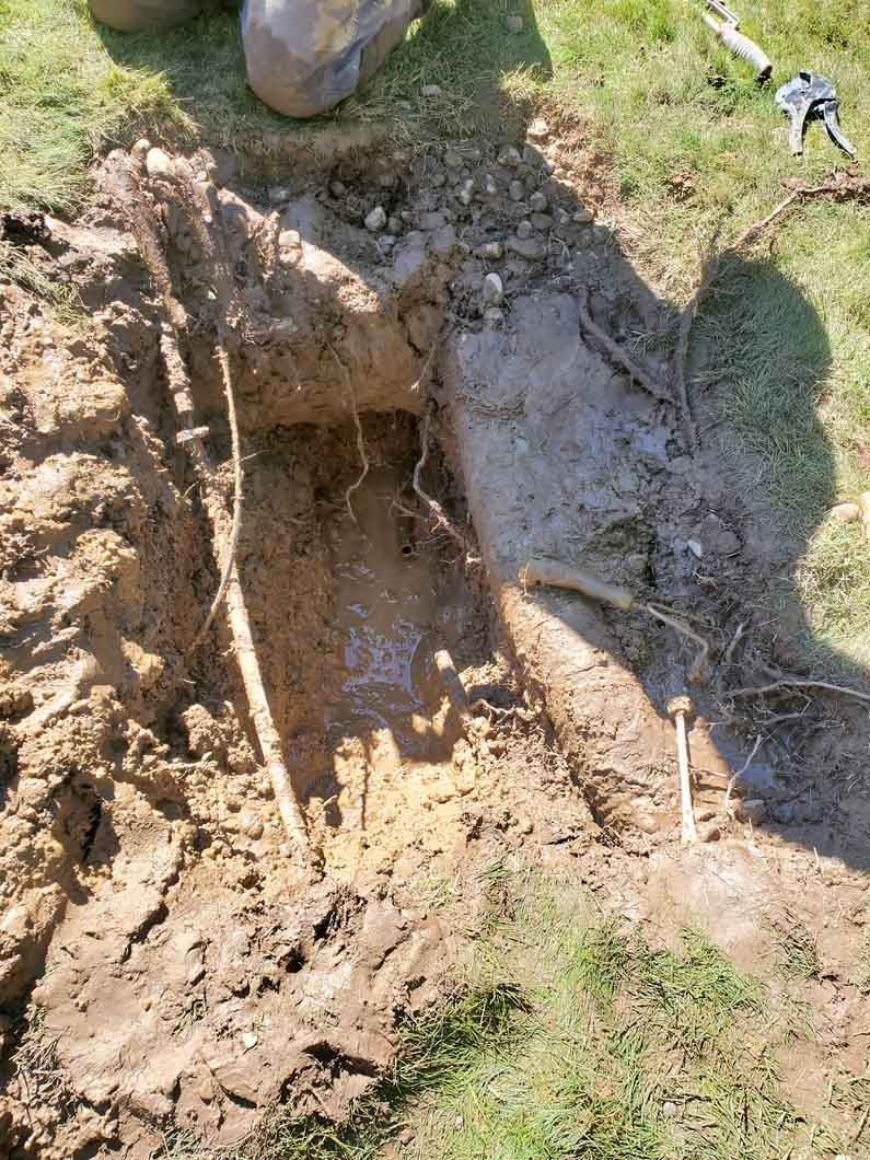 Mud-filled hole in the ground with a person's boots visible at the top edge