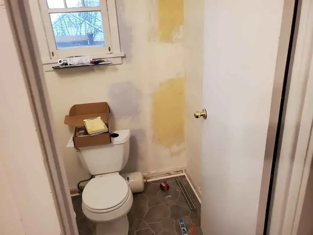 Small bathroom under renovation with a toilet, unfinished walls, and construction tools on the floor.