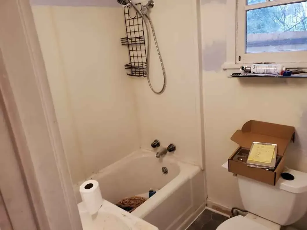 Small bathroom with a bathtub, toilet, shower caddy, and a toilet paper roll on the tub edge.