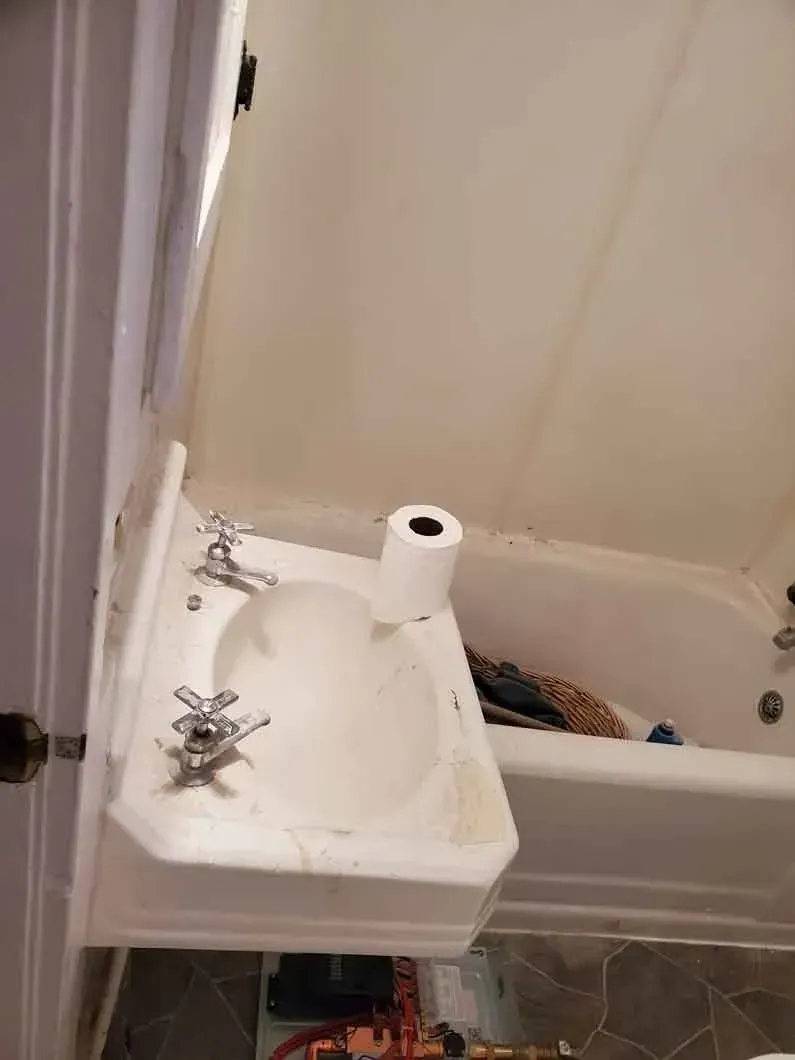 Small white wall-mounted sink beside a bathtub in a bathroom, with a soap dispenser on the tub edge.