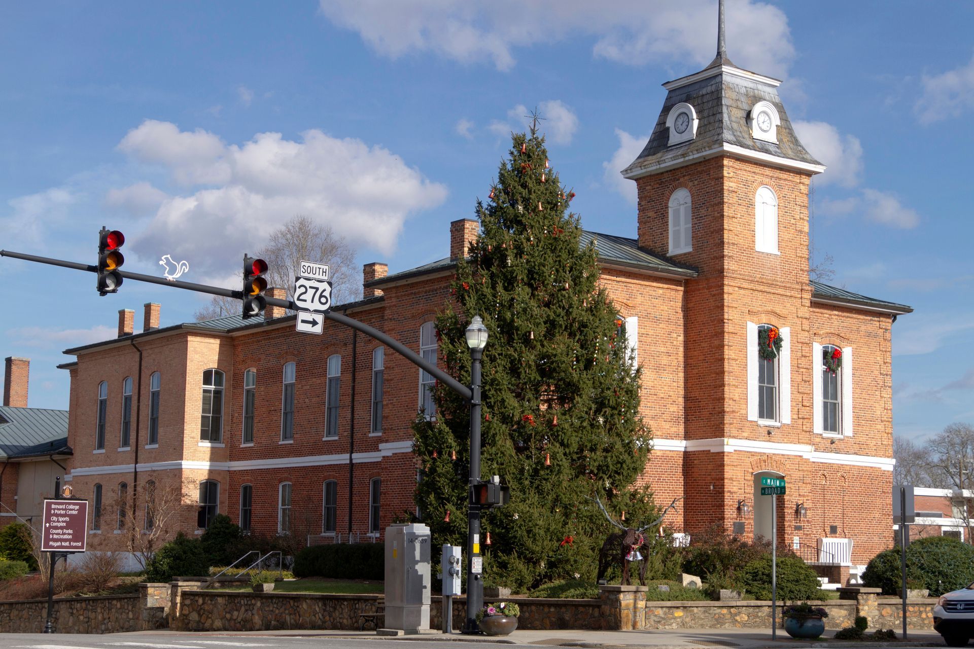 Brick civic building with a clock tower beside a traffic light under a blue sky