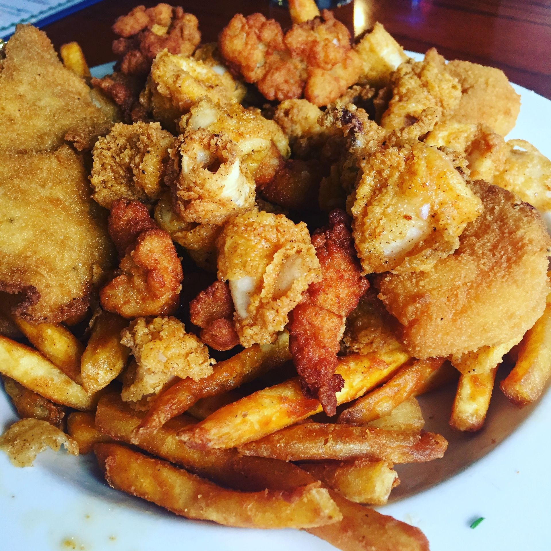 Fried fish and fries on a white plate, topped with golden crumbs and sauce
