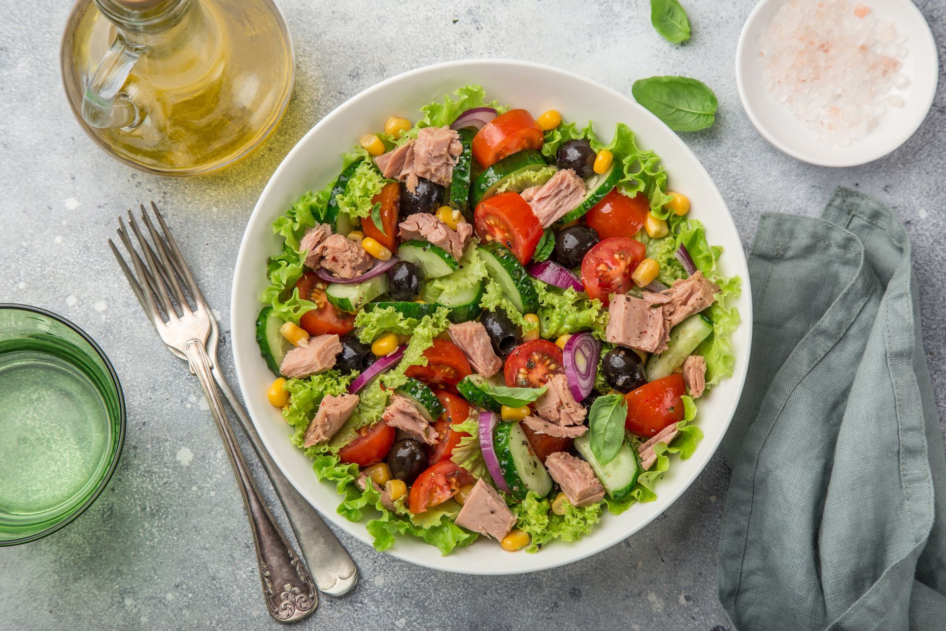 Salad bowl with tuna, avocado, tomatoes, cucumber, and peas on a gray table with dressing and a fork