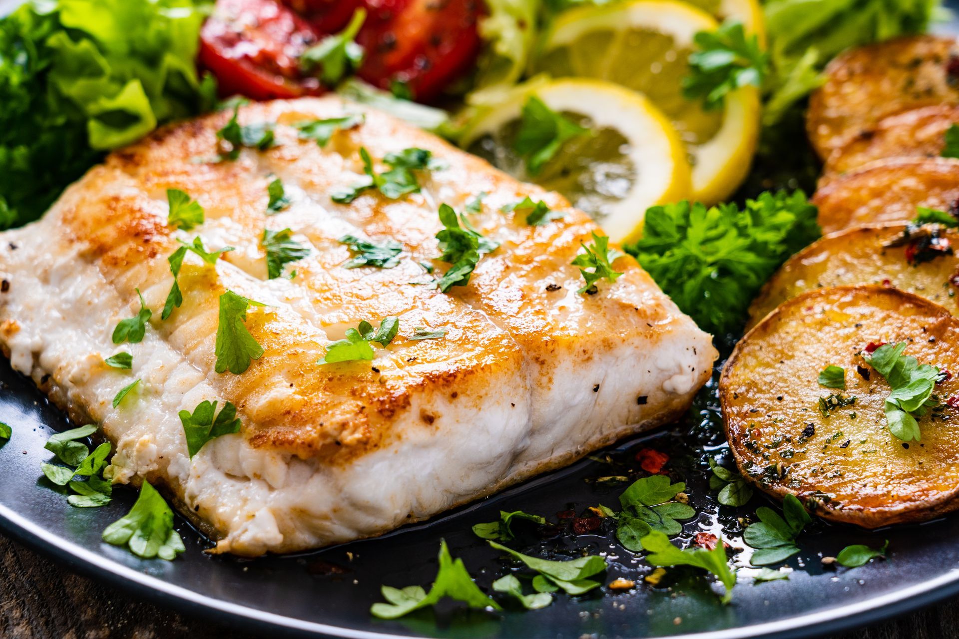 Grilled fish fillet with lemon, parsley, and roasted vegetables on a dark plate