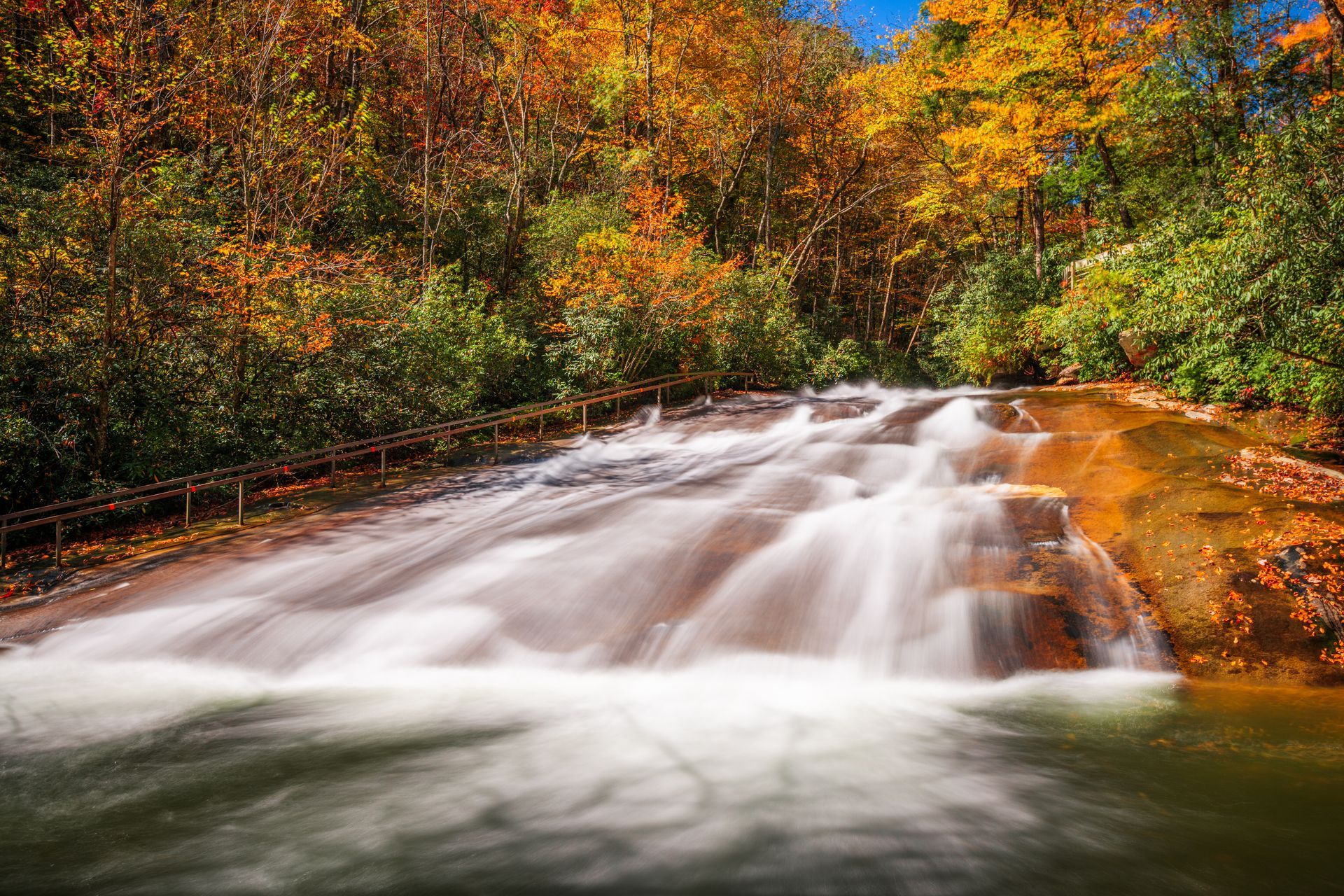 Autumn waterfall flowing over rocks beneath colorful orange and green trees