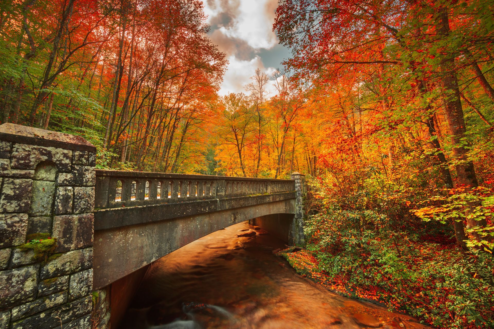 Stone bridge over a stream in an autumn forest with vivid red, orange, and yellow leaves