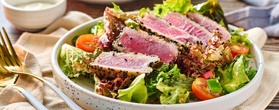 Seared tuna salad with mixed greens, tomatoes, and dressing in a white bowl
